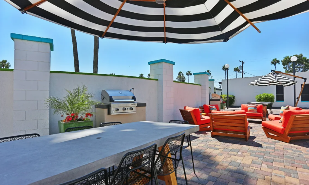A patio with a table, chairs, and a grill under a striped umbrella. at Palm Villas, Scottsdale