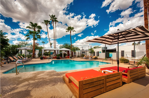 Resort style pool with striped umbrella and loungers at Palm Villas Apartments, Arizona