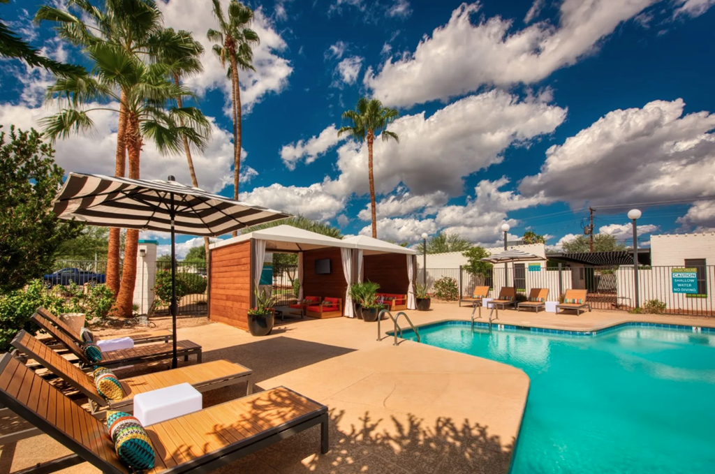 A pool area with a sun lounger and a striped umbrella. at Palm Villas, Scottsdale, 85257