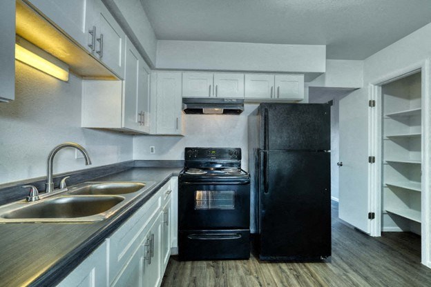 A black refrigerator stands in a kitchen with white cabinets and a stainless steel sink. at Connect on University, Mesa, AZ, 85203