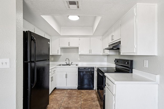A kitchen with black and white appliances and brown tile flooring.