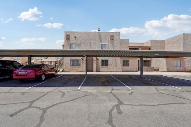 A parking lot with a building in the background and a red car parked in the lot.