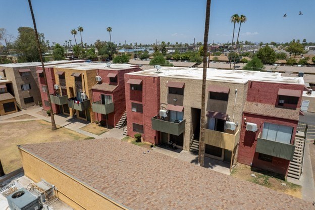 Apartment complex with red and beige buildings and palm trees in the background.