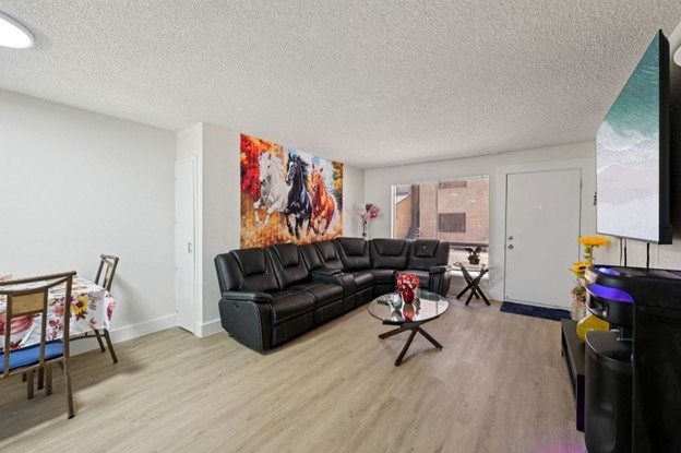 A living room with a black leather couch and a painting on the wall.