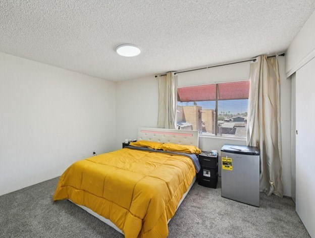 A bedroom with a yellow bedspread and a window showing a red roof.