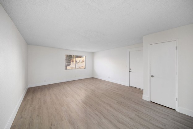 A room with white walls and wooden flooring with a window.