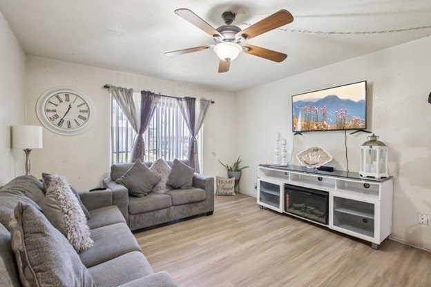 A living room with a grey couch, a white entertainment center, and a ceiling fan.