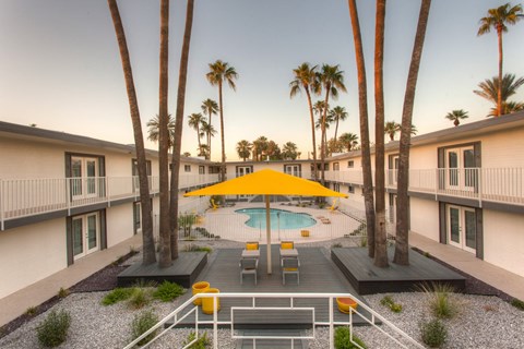 A community pool surrounded by palm trees and a yellow umbrella.