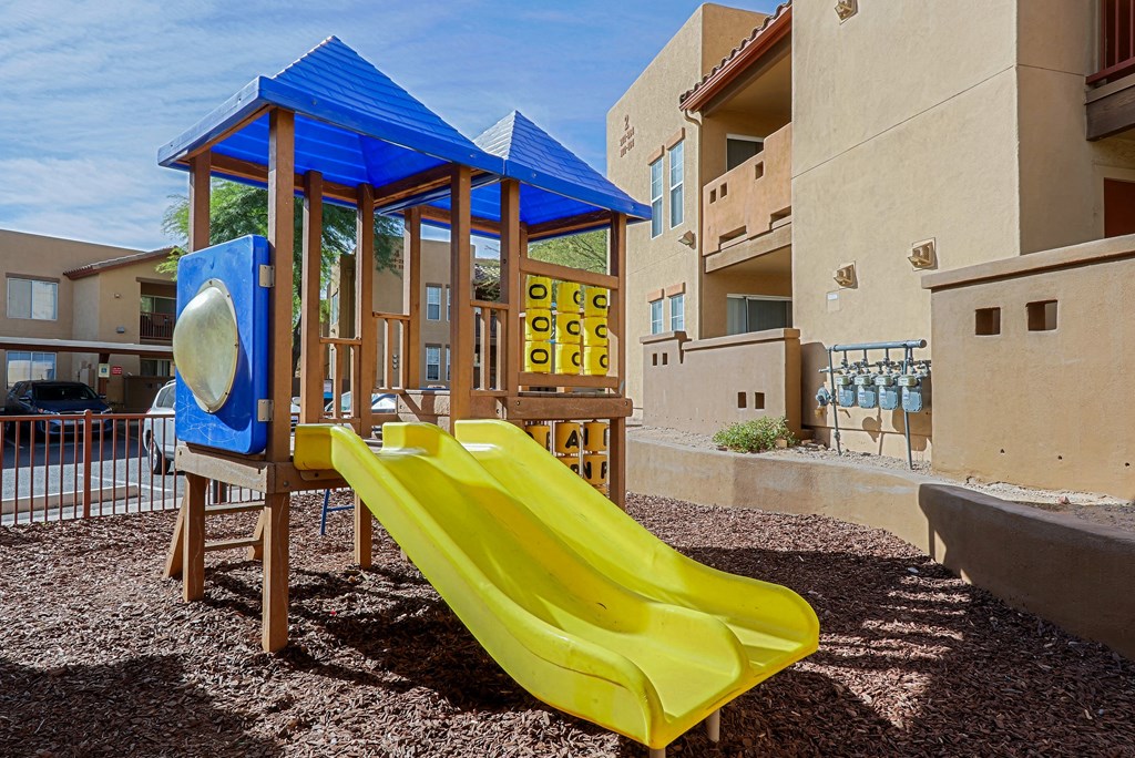 A playground with a yellow slide and a blue canopy.