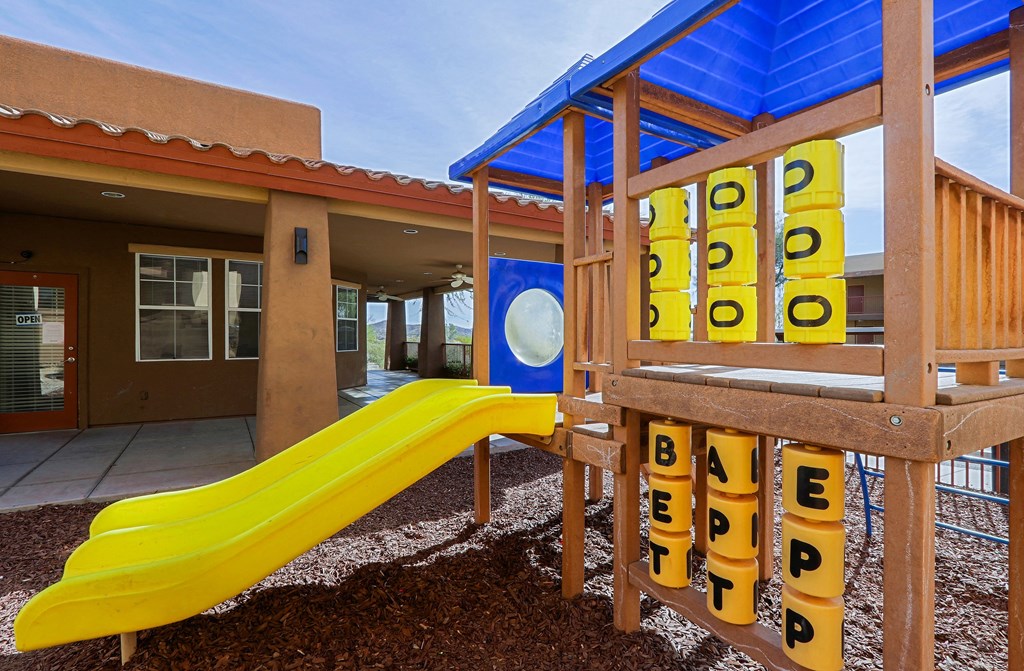 A playground with a yellow slide and a wooden structure with the word "BETTER" spelled out on it.