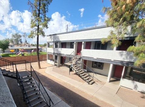 A white building with a red door and a tree in front.