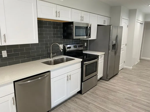 A kitchen with white cabinets and a black backsplash.