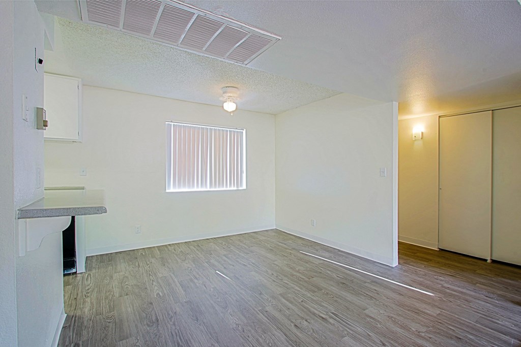 the living room and dining room of an apartment with wood flooring and a window
