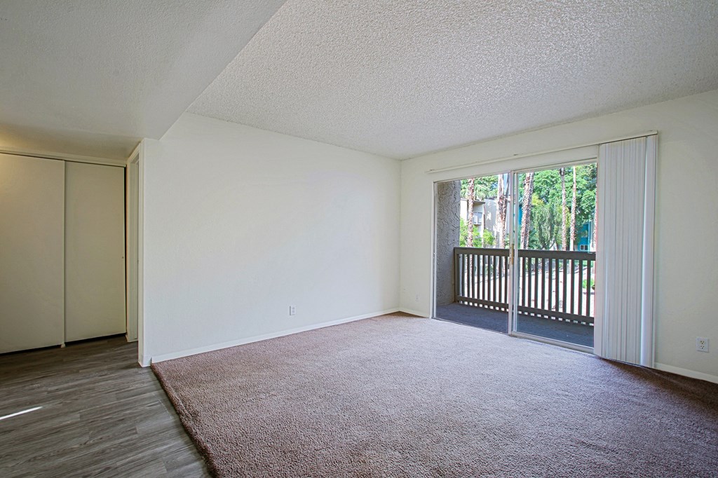 an empty living room with a sliding glass door to a balcony