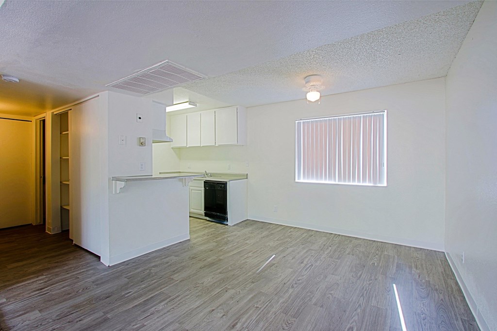 the living room and kitchen of an apartment with white walls and wood flooring
