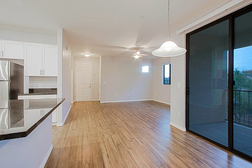 an empty living room with a sliding glass door to a kitchen