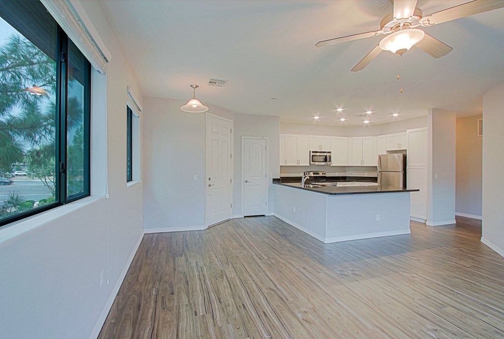 an empty living room with a kitchen and a ceiling fan