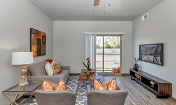 Living room with plank flooring, sliding glass doors that lead to the balcony, grey lounge chairs and couch, and high ceilings at Allora Phoenix in Arizona, 85021