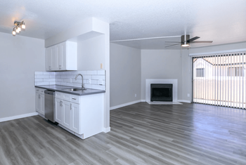 Spacious living room with plank flooring, sliding glass doors that lead to the patio, view into kitchen, and fireplace at Tides at Mesa, Mesa, 85204