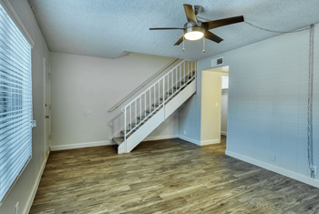 Living room with a ceiling fan, oversized windows, plank flooring, and carpeted staris leading to second level at Connect on Missouri in Arizona 85015