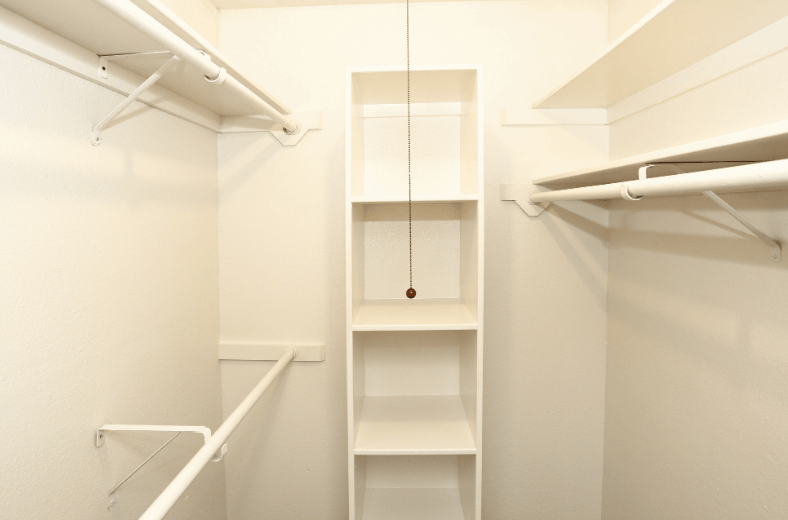 a walk in closet with white shelves and a hanging closet organizer