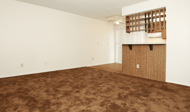 an empty living room with carpet and a kitchen