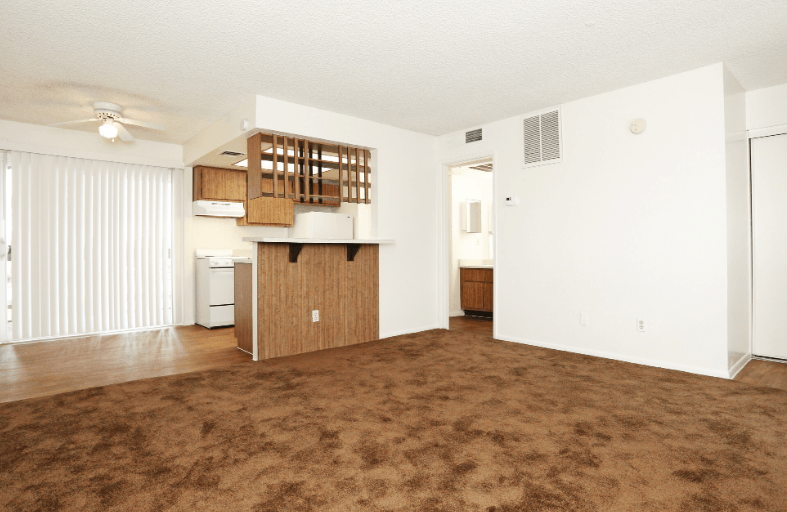 an empty living room with a kitchen in the corner