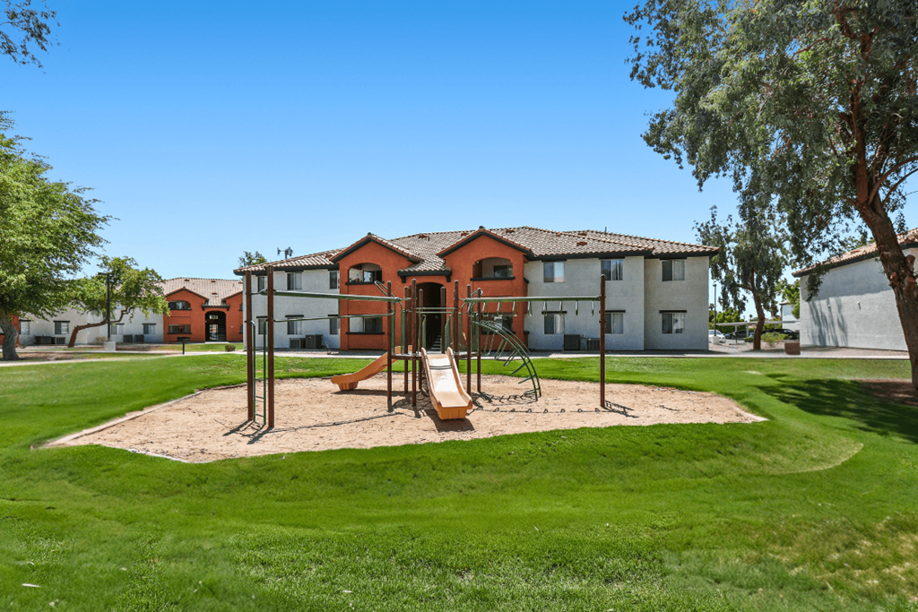 A playground with a swing set and sandbox in front of a building.