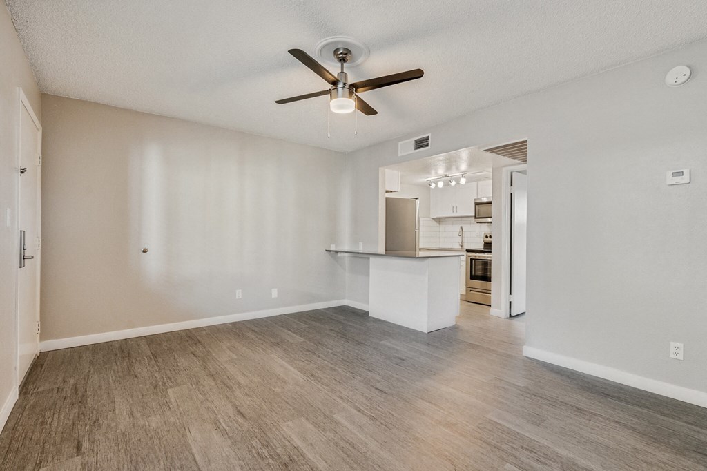 A spacious room with a ceiling fan and light fixture, and a kitchen area visible through the open door at Tides on East Cactus Apartments, Phoenix, Arizona