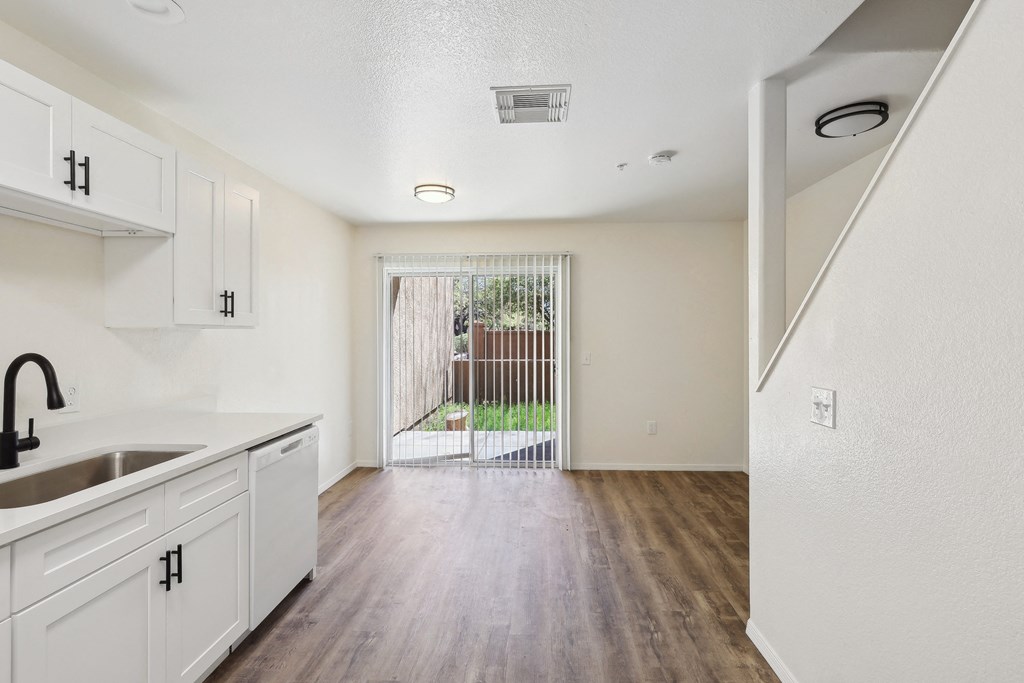 the living room and kitchen of an apartment with white cabinets and wood flooring