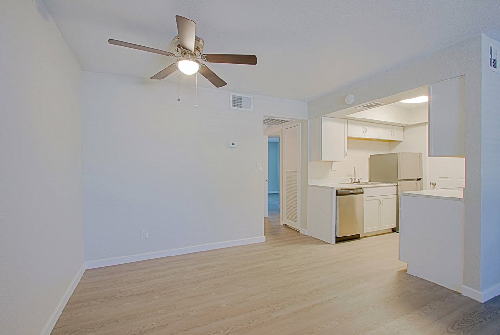 an empty living room with a ceiling fan and a kitchen