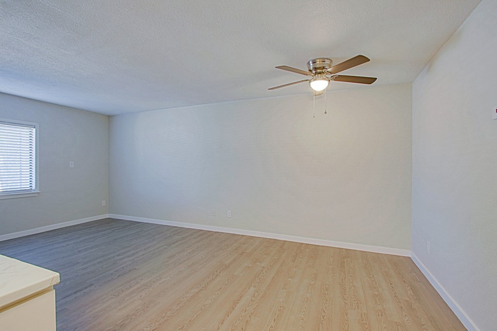 the spacious living room of an empty home with a ceiling fan