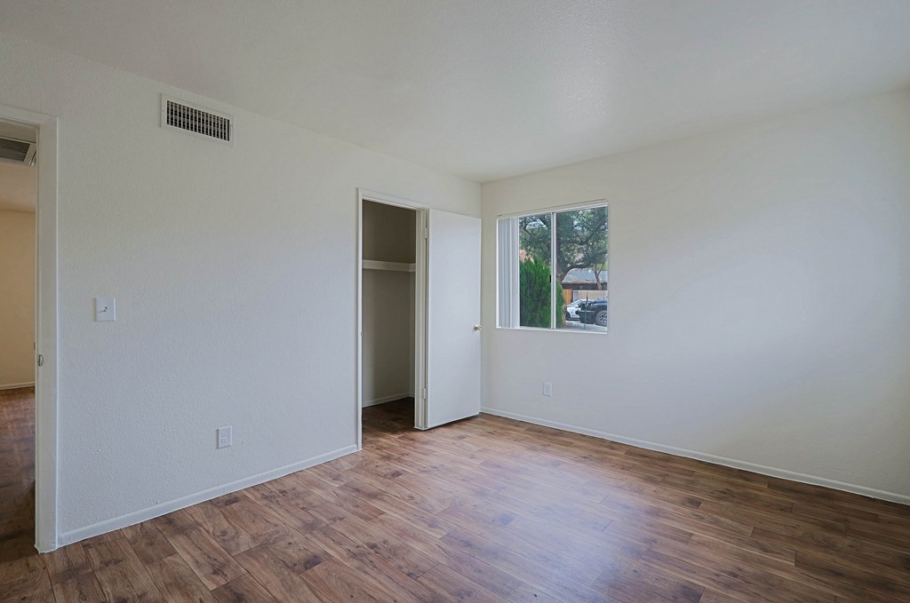 A room with a wooden floor and a window showing trees outside.