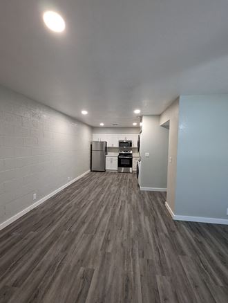 an empty living room with wood floors and a kitchen