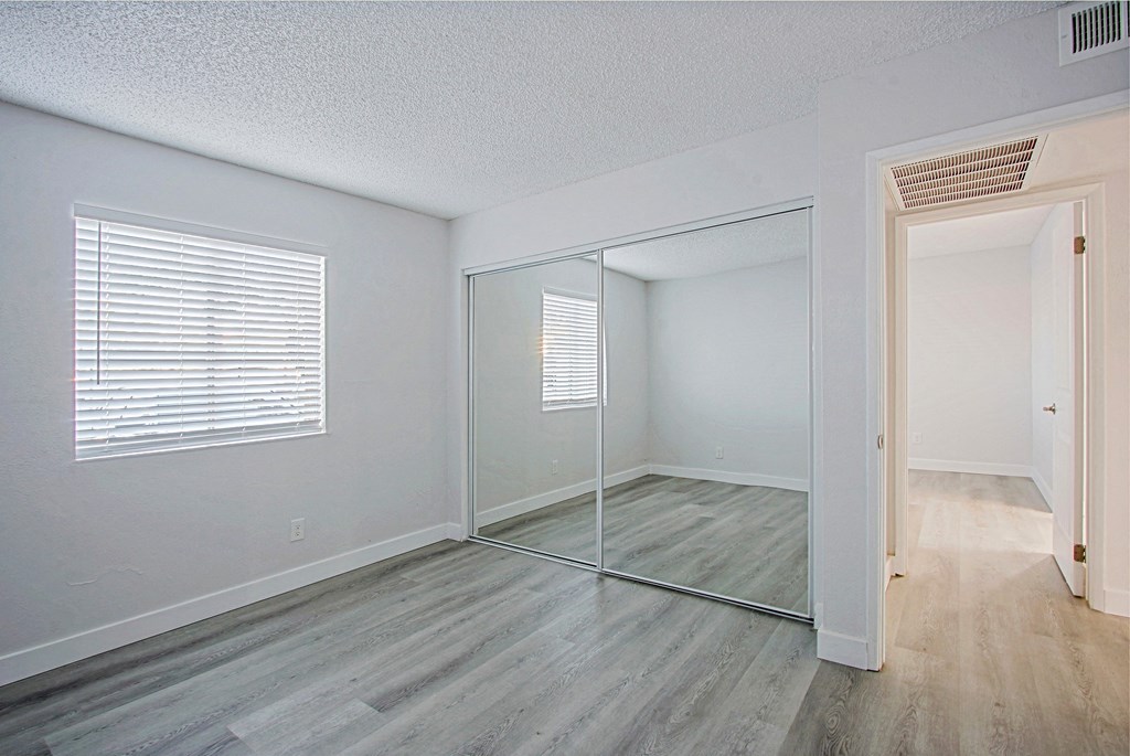 an empty bedroom with a mirrored closet and a large window