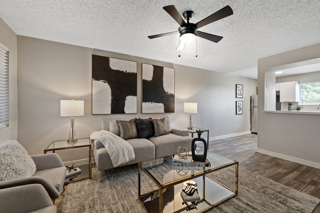 A living room with a grey couch, a glass coffee table, and a ceiling fan.