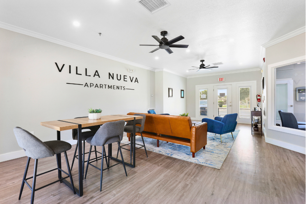 A living room with a dining table and chairs in front of a wall that says "VILLA NUEVA APARTMENTS".
