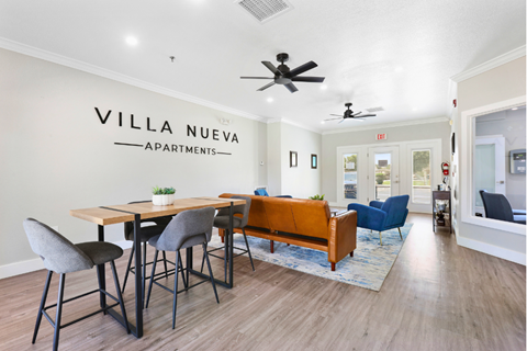 A living room with a dining table and chairs in front of a wall that says "VILLA NUEVA APARTMENTS".