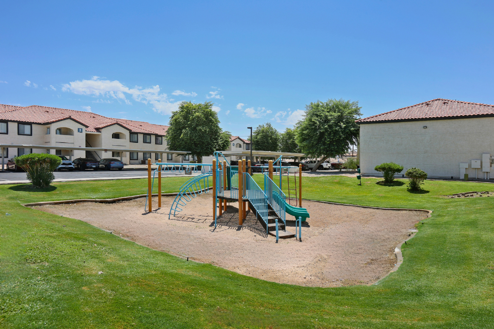 A playground with a green slide and a blue slide in the middle of a sand pit.