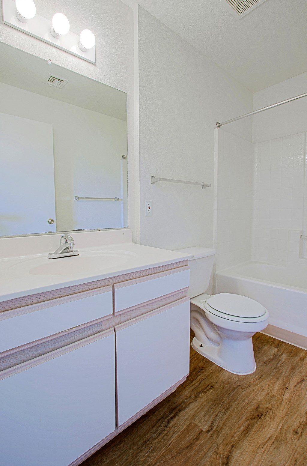 A white toilet sits in a bathroom with a white sink and a large mirror.
