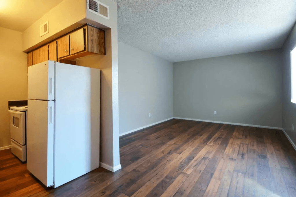 A white refrigerator is in a room with wood floors at Gilbert Square Apartments, Mesa