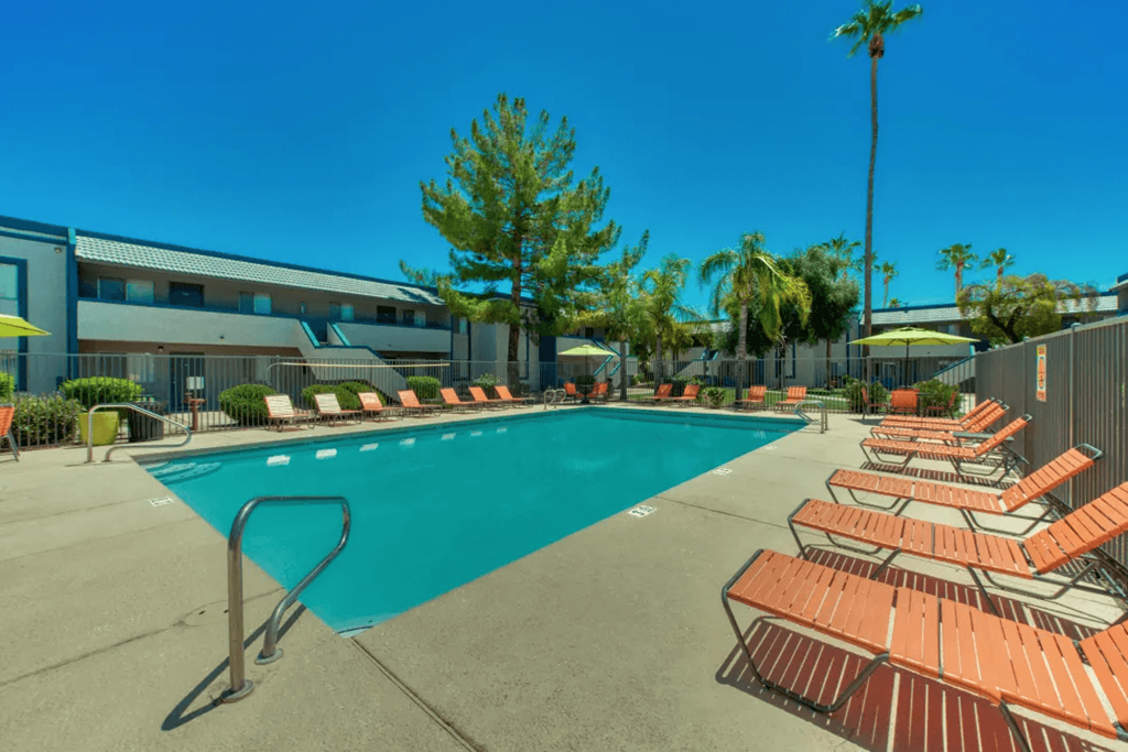 A pool surrounded by sun loungers and palm trees at Gilbert Square Apartments, Mesa, 85203