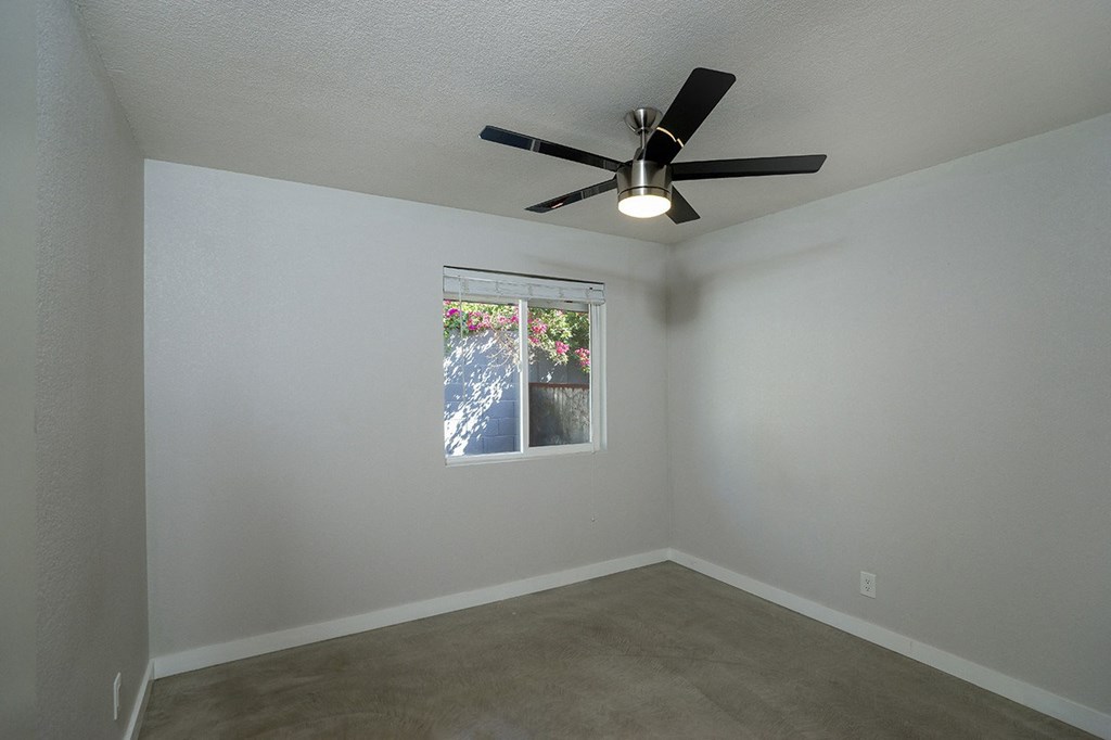 an empty living room with a ceiling fan and a window
