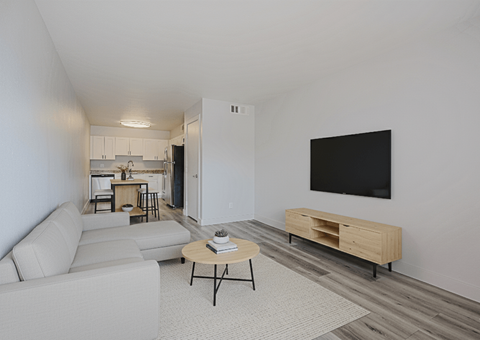 A living room with a white couch, a coffee table, and a TV mounted on the wall.