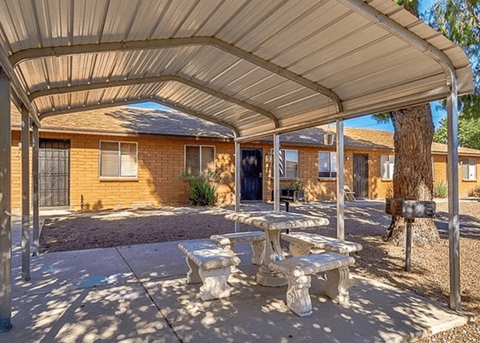 a covered patio with picnic tables in front of a yellow house