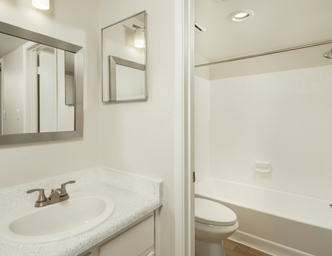 A white bathroom with a sink, mirror, toilet and bathtub.