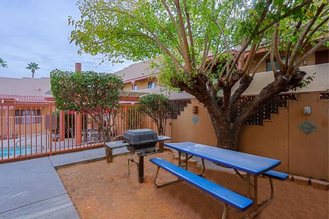 A blue picnic table is in front of a tree and a building.