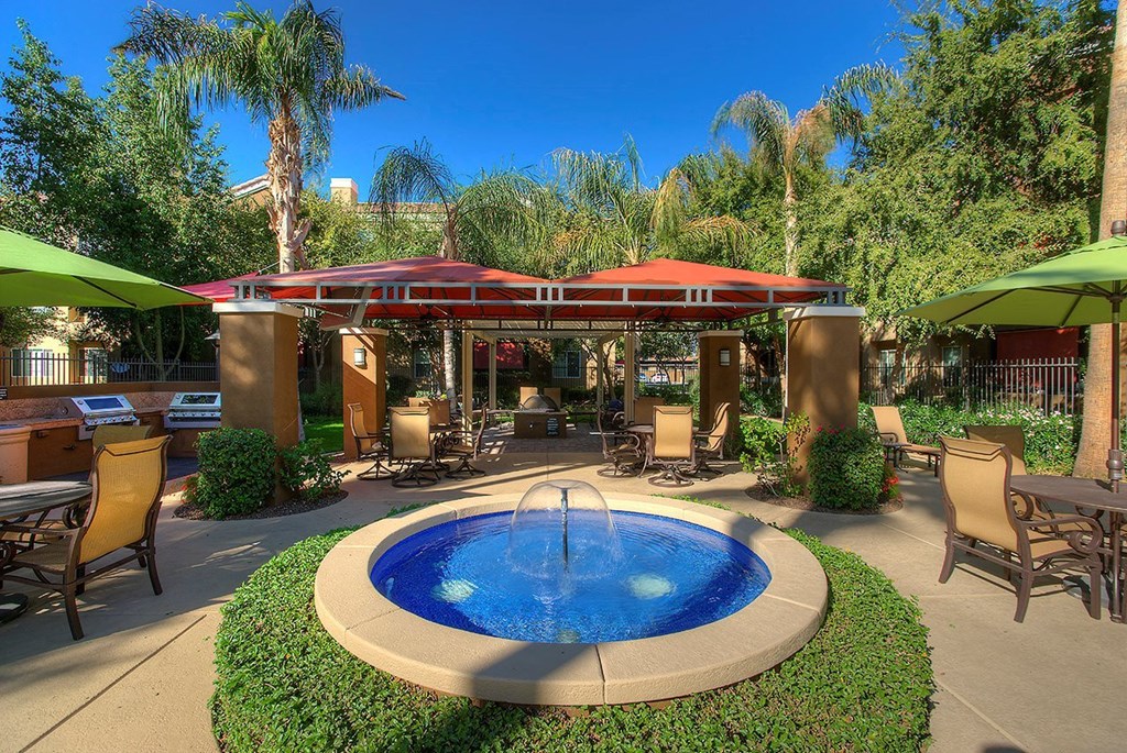a pool with a fountain in a courtyard with tables and umbrellas