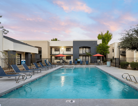 A swimming pool surrounded by lounge chairs and a building in the background.