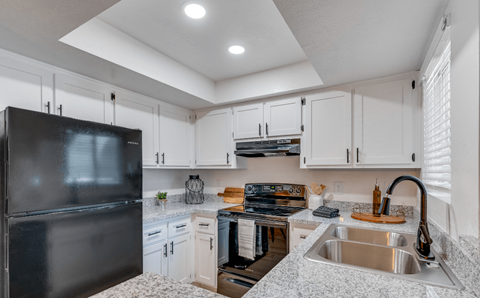 A kitchen with a black refrigerator and white cabinets.